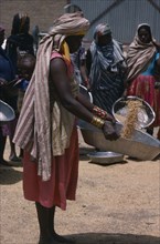 SUDAN, Work, Nigerian woman with child in sling on her back winnowing grain.