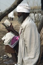 SUDAN, Religion, Amhara Ethiopian orthodox priest reading from book in refugee settlement.