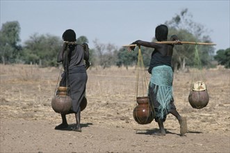 SUDAN, Habila Settlement, Chadian refugee women carrying water vessels hanging from pole across
