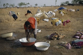 GHANA, Laundry, Laundress washing clothes in bowls with garments spread out over bushes to dry
