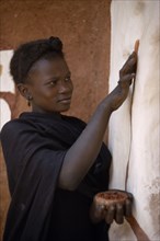 MAURITANIA, Oualata, Young woman decorating exterior wall of mud building with ochre.  It is