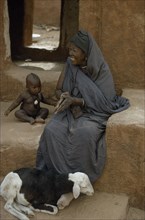 MAURITANIA, Oualata, Portrait of woman sitting beside young child with sheep at her feet.