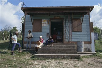 WEST INDIES, Jamaica, Local store with people standing beside and sitting on steps to entrance.
