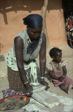 KENYA, People, Women, Burji woman grinding grain on large flat stone to produce flour with child