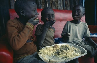 KENYA, Children, Three young children using right hands to eat Christmas lunch.