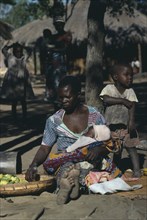 ZAMBIA, Ukwimi Settlement, Mozambique refugee woman and children with basket of fruit.
