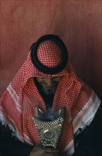 QATAR, Tribal People, Portrait of Bedouin man inside tent looking down at studded leather artefact.