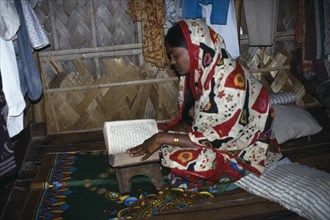 BANGLADESH, Religion, Islamic, Woman reading the koran in home in slum area.