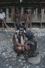 INDONESIA, Irian Jaya, Baliem Valley, Dani Warrior man holding smoked ancestral mummy with three