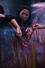 CHINA, Guangzhou, People, Young woman lighting incense at temple.