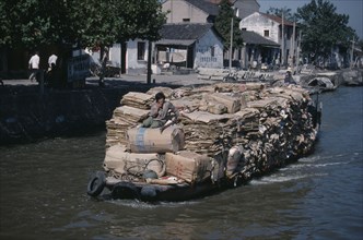 CHINA, Jiangsu Province, Suzhou, Man on boat travelling along the Grand Canal carrying piles of