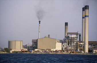 CURACAO, Willemstad, Seawater desalination plant exterior with narrow chimney emitting black smoke.