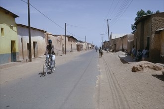 NIGERIA, Kano, Street scene in old city with cyclist on road lined with mud brick architecture.