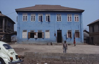 NIGERIA, Inagbiji, Blue painted exterior of typical house with wooden shutters and children in yard