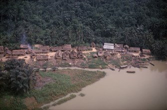 NIGERIA, Rivers State, Aerial view over thatched village on river bank beside area of tropical