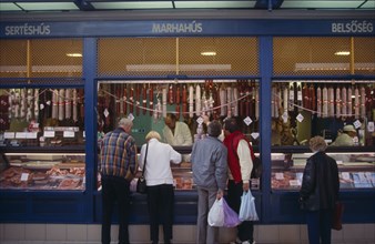 HUNGARY, Budapest, Tourists buying salami from butchers with counter open on to street.