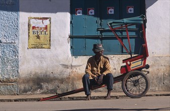 MADAGASCAR, Ambalavao, Man sitting on his rickshaw awaiting a fare at the side of the road with a