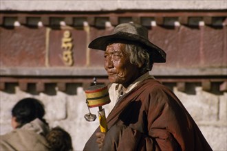 CHINA, Tibet, Lhasa, An elderly pilgrim with prayer wheel in the Barkhor Bazaar