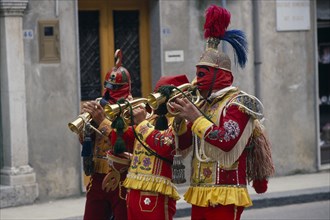 ITALY, Sicily, San Fratello, Bugle players wearing red and yellow costumes and masks celebrating