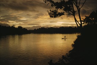 COLOMBIA, Choco Region, Noanama Tribe, Boy paddling canoe on lower rio San Juan at sunset