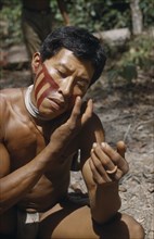 COLOMBIA, Vaupes Region, Tukano Tribe, "Man applies red “karajuru” facial paint, wearing precious