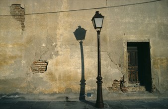 SPAIN, Madrid, Street lamp casting shadow against cracked and peeling plaster wall.