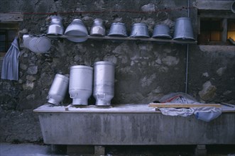 SWITZERLAND, Agriculture, Washed milk churns and pails on shelf above trough.