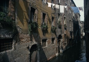 ITALY, Veneto, Venice, "Canalside houses with crumbling plaster and brickwork, plants and flowers