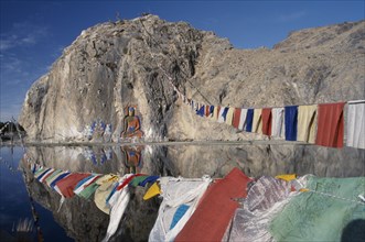 CHINA, Tibet, "Carved Buddha, Buddhist paintings and prayer flags on a rock wall by the road from