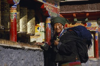 CHINA, Tibet, Sakya, A pilgrim turning prayer wheels outside the monastery.