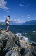 SWITZERLAND, Vaud, Lake Geneva, Fisherman standing on rocks at the entrance to Lutry Marina.