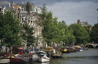 HOLLAND, Amsterdam, Canal and moored houseboats and barges overlooked by traditional architecture.