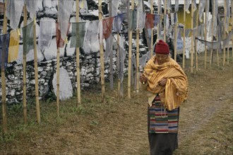 INDIA, Sikkim, Tashiding, "A pilgrim holding a prayer wheel and beads, walking past a mani wall and