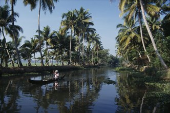 INDIA, Kerala, Near Kumarakom. A single person paddling in a local boat on the backwaters.