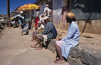 MADAGASCAR, Ambositra, A group of local people sat on a wall waiting at the side of the road
