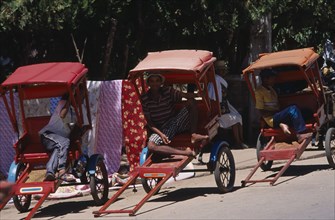 MADAGASCAR, Ambositra, Men drivers sitting in the shade of their Rickshaws waiting for a fare