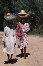MADAGASCAR, People, Women, Near Ambositra. Two barefooted women walking up a dirt track carrying