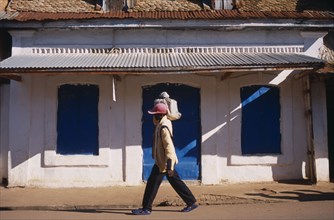 MADAGASCAR, Ambalavao, Boy wearing a red cap carrying a bag on top of his shoulder walking past a