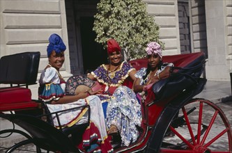 CUBA, Havana, Three woman tourist dancers dressed in costume sat in a horse carriage
