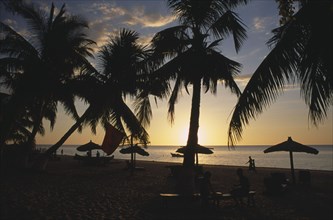 MADAGASCAR, Tulear, Ifaty Beach at sunset with view through palm trees and straw sun shades towards