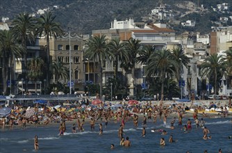 SPAIN, Catalonia, Stiges, Busy resort near Barcelona.  Crowded beach with palm trees and seafront