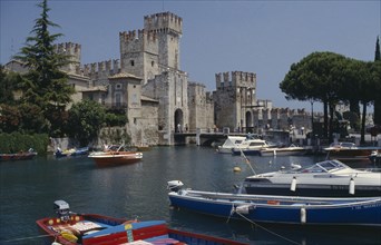 ITALY, Lombardy, Lake Garda, Sirmione castle with boats moored on the lake in the foreground.