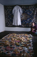 TAJIKISTAN, Wedding, "A white wedding dress hangs on the wall in front of a rug, and a large