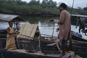 NIGERIA, Bonny, Fisherman and young girl untangling nets in wooden canoes.