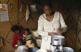 SOUTH AFRICA, People, Poor family in interior of home with woman cooking over gas ring.