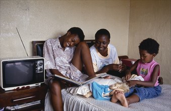 SOUTH AFRICA, Gauteng, Alexandra Township, "Three girls relaxing in bedroom of home.  Two eldest
