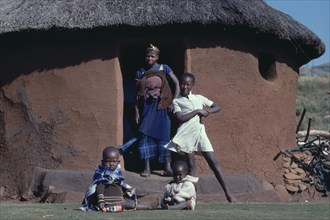 SOUTH AFRICA, Kwazulu Natal, "Mother and children in doorway of thatched, mud brick home."