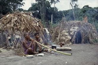 CONGO, Ituri Forest, "Pygmy women smoking tobacco outside thatched, domed huts."