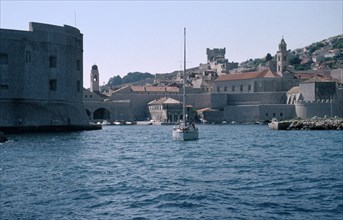 CROATIA, Dalmatia, Dubrovnik, The Old City harbour with stone fort and a yacht sailing on the water
