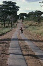 ZIMBABWE, Garooma, Cyclist carrying passenger on the crossbar on strip tar road
